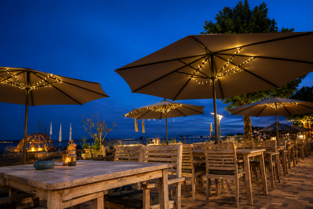 Het terras van The Beach Huizen bij schemering, met parasols en warme lichtjes